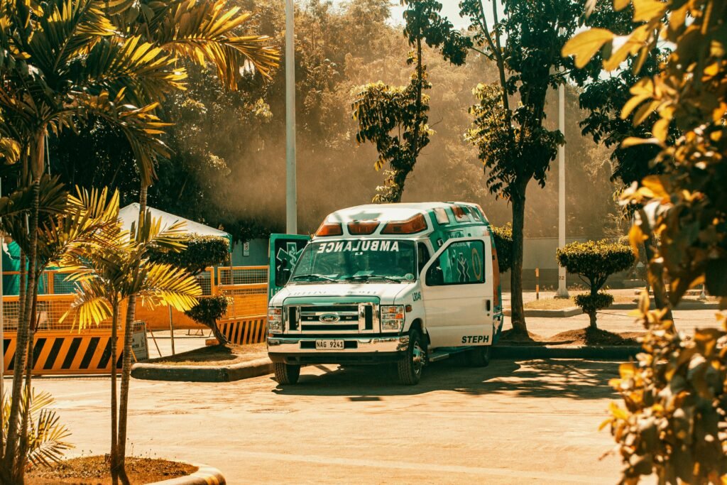 A parked ambulance in a sunny outdoor space, surrounded by trees and urban elements.