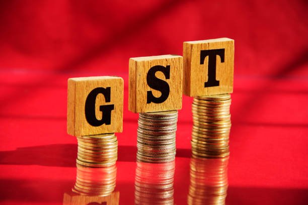 wooden-letters-gst-and-money-coin-stack-on-red-table-background-financial-concept.jpg